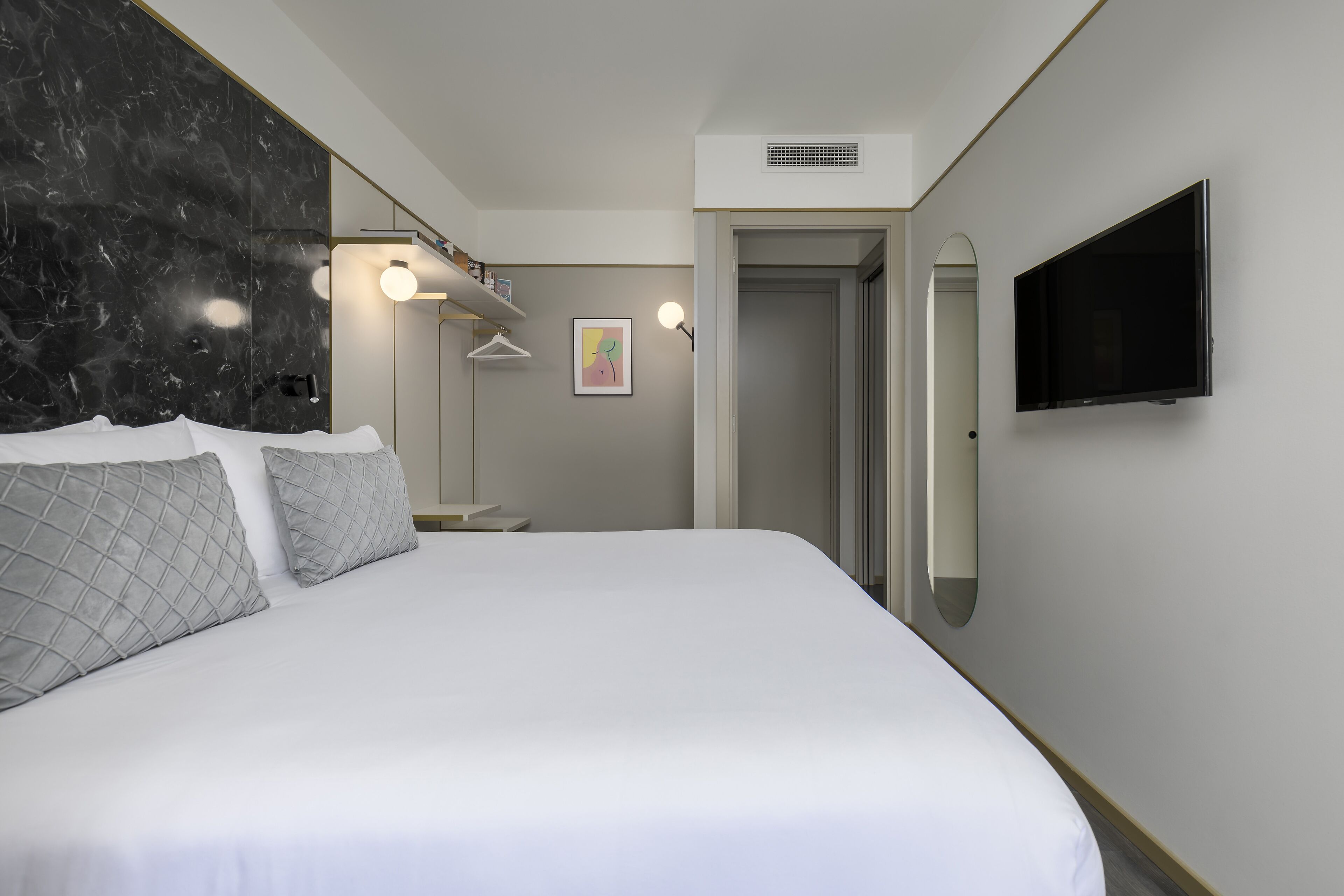 Ein modernes Hotelzimmer mit einem großen Bett, einem Flachbildfernseher, einer Marmorwand und einem minimalistischen Design.