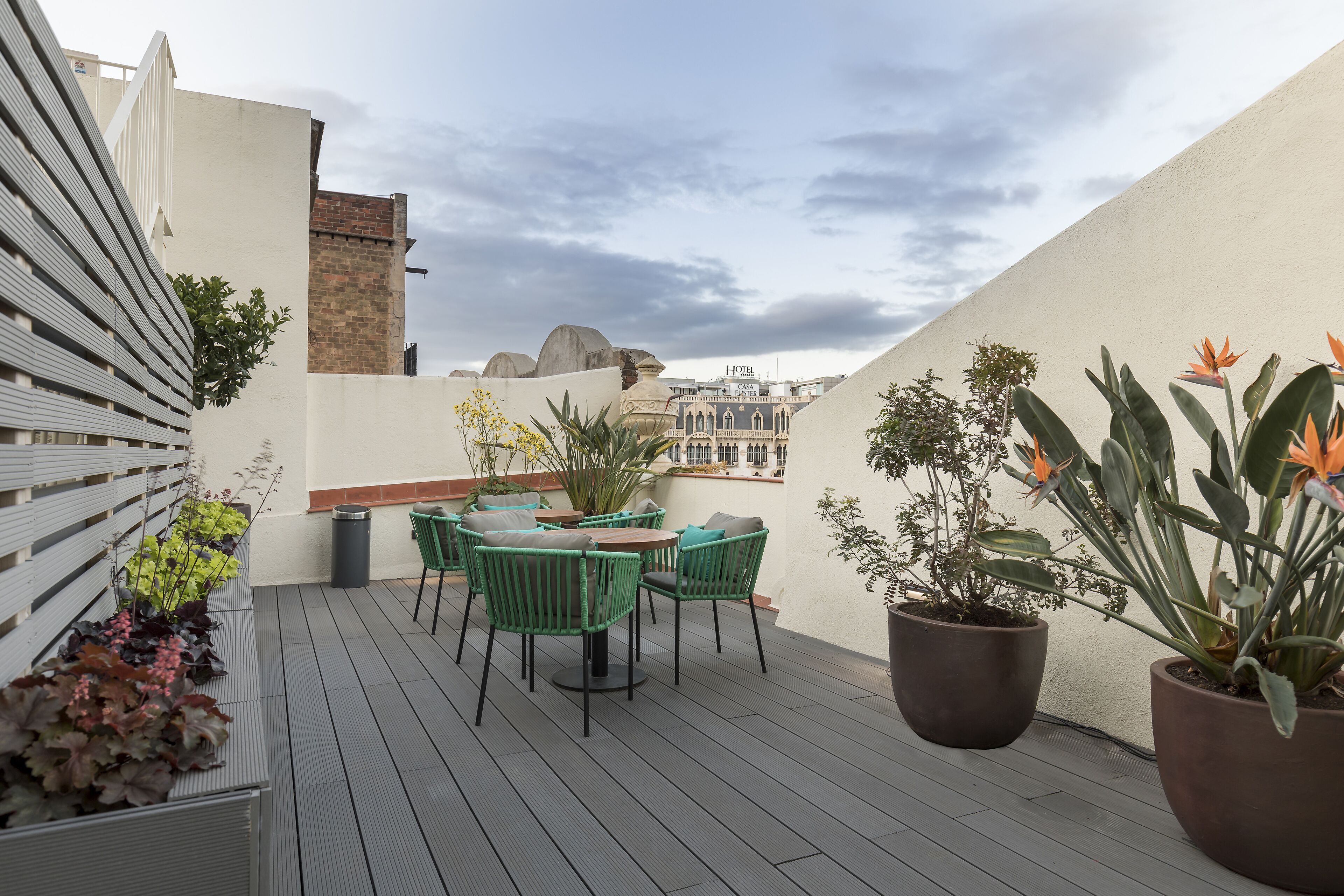 Una terraza en la azotea con zona de estar, plantas en macetas y vistas panorámicas de la ciudad.