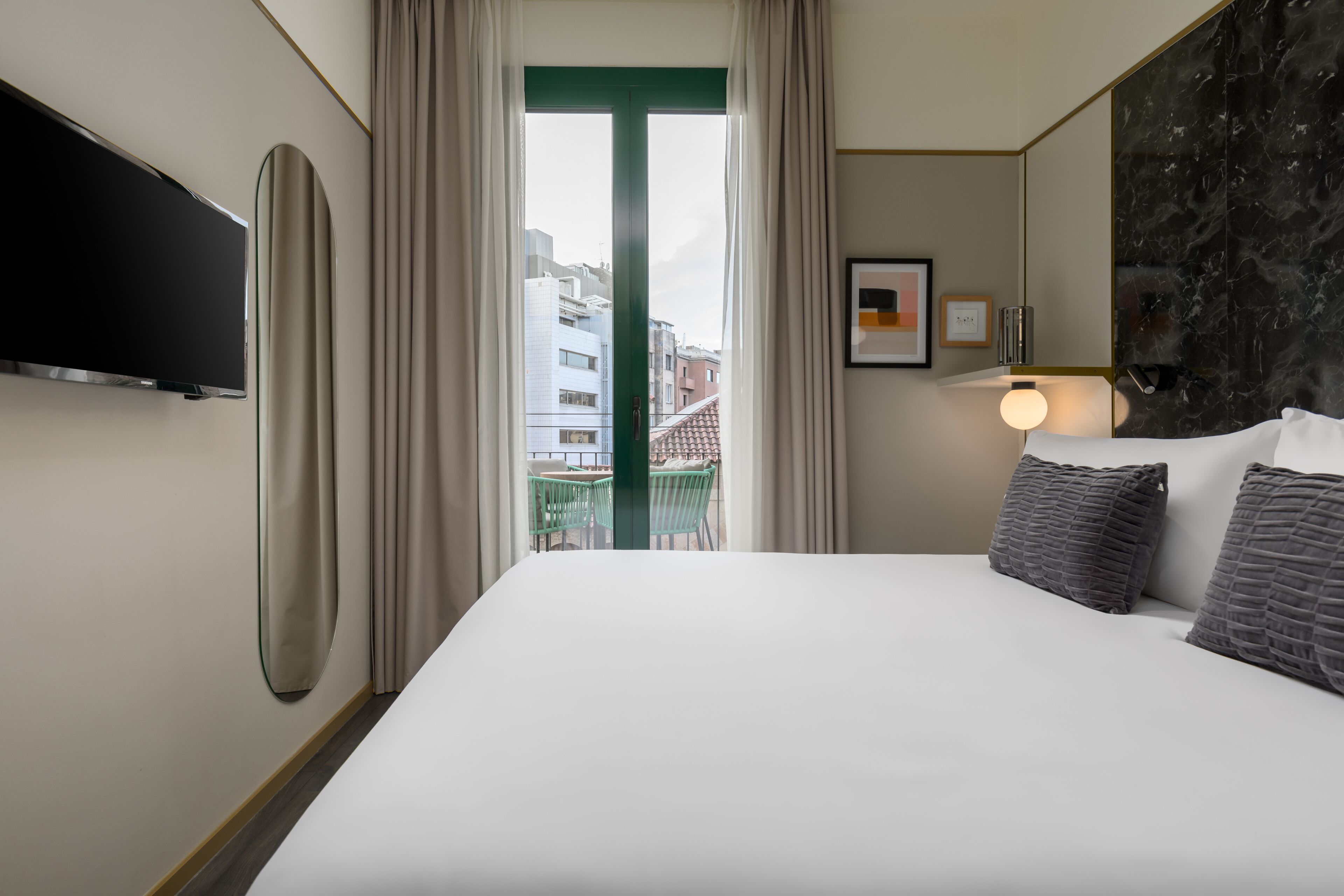 A hotel room with a bed, a TV, a balcony view, and a wall-mounted light fixture.