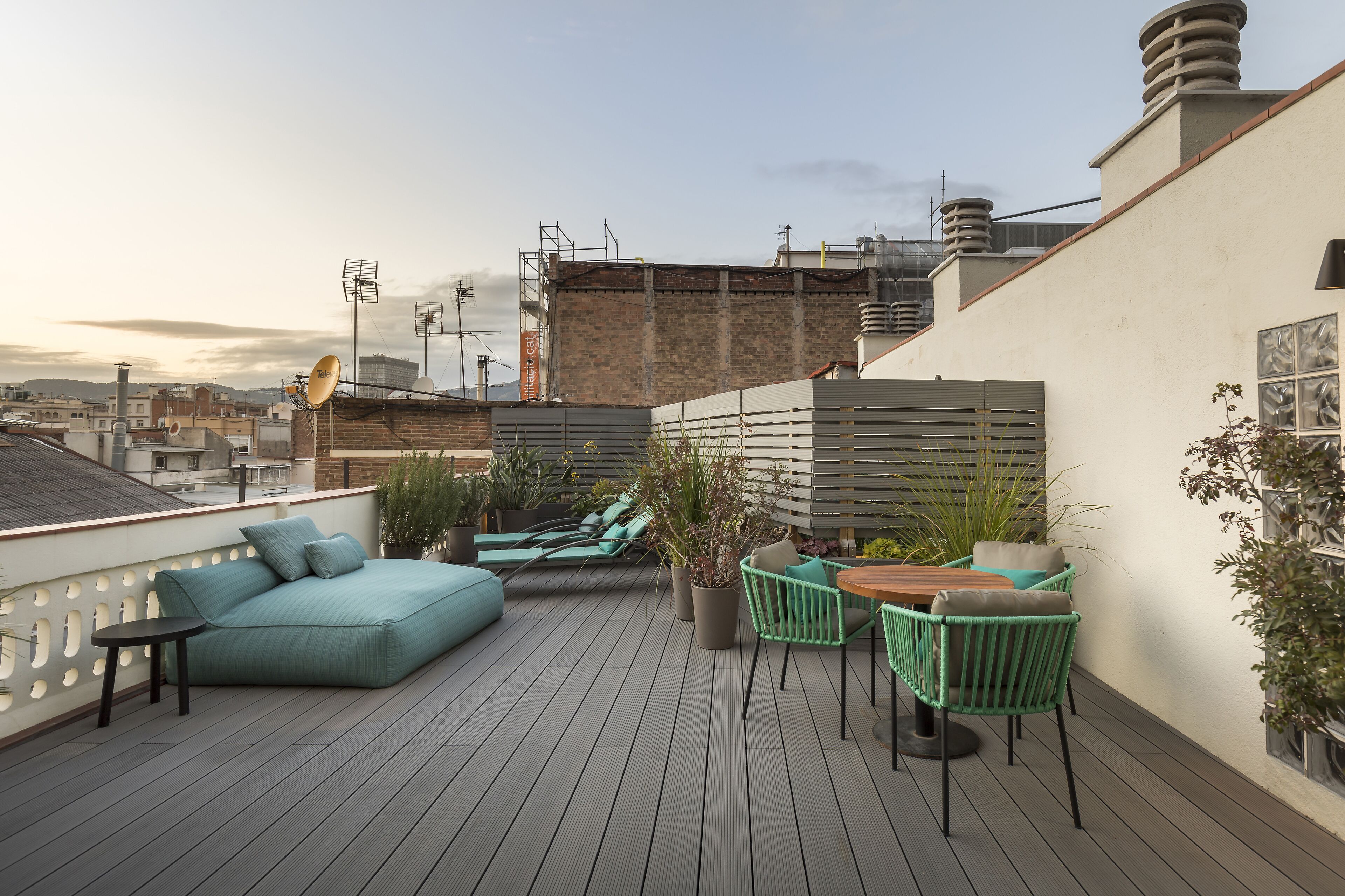 A rooftop terrace with a sofa, chairs, and a table, surrounded by potted plants.