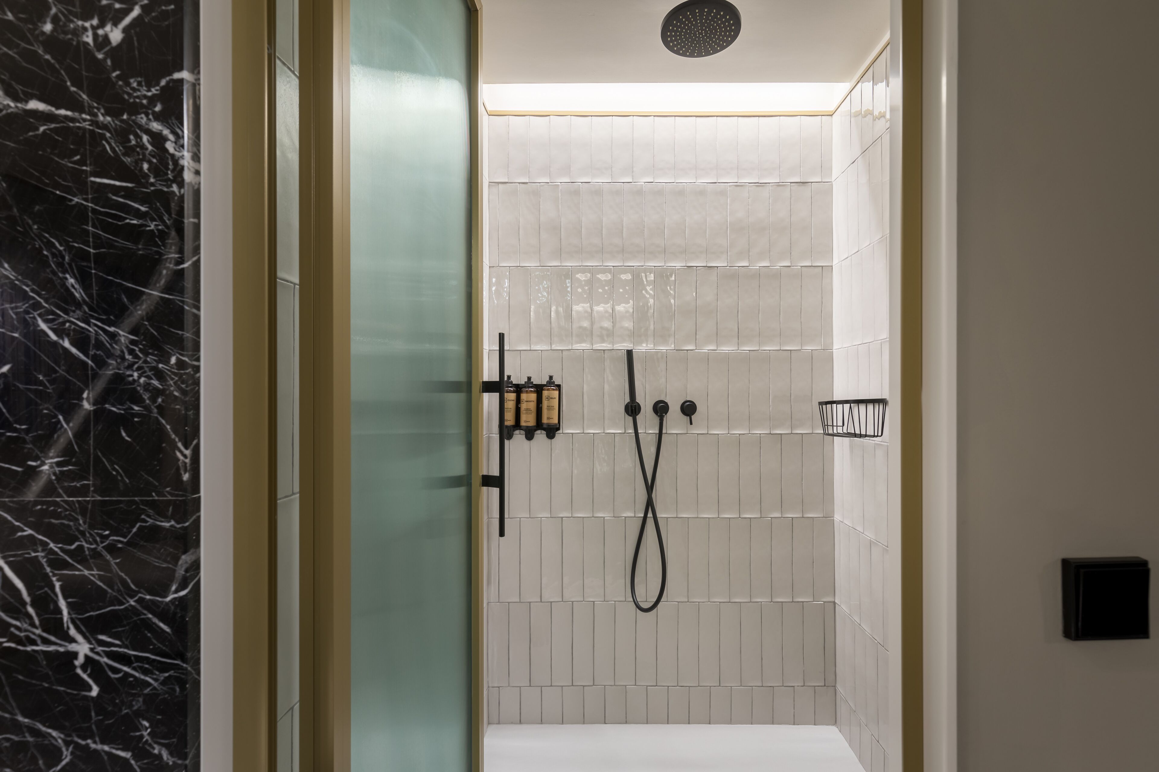 A modern bathroom with a glass door, white tiled walls, and a black marble accent wall.