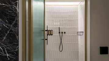 A modern bathroom with a glass door, white tiled walls, and a black marble accent wall.