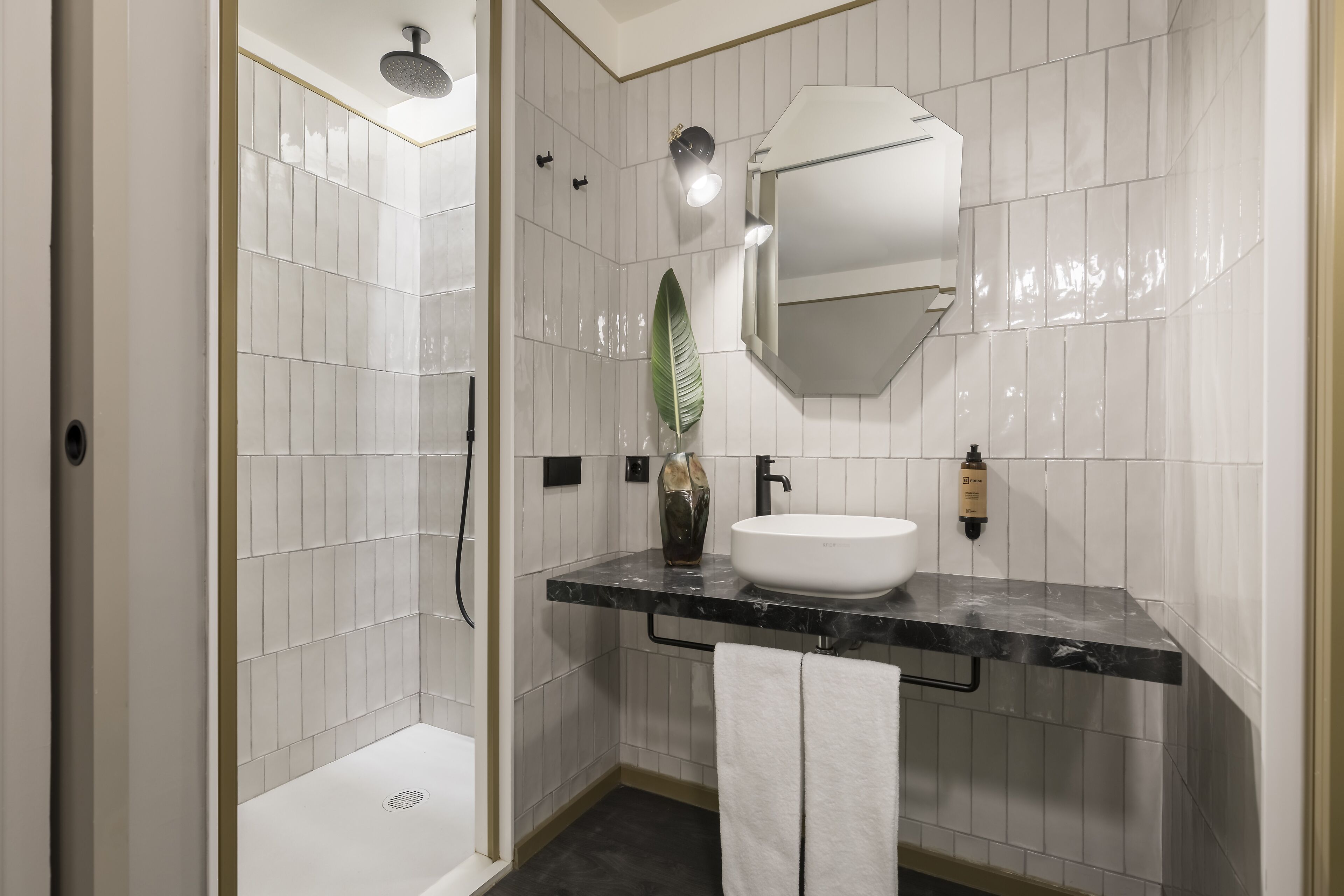 Une salle de bain moderne avec une douche carrelée de blanc, un lavabo en marbre noir et un grand miroir.
