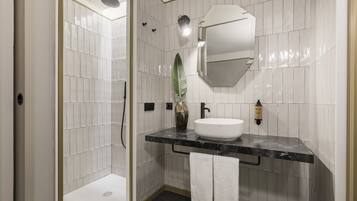 Une salle de bain moderne avec une douche carrelée de blanc, un lavabo en marbre noir et un grand miroir.