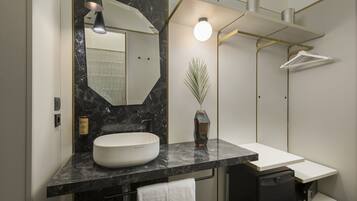 A modern bathroom with a large mirror, a white sink, a black marble countertop, a towel rack, and a shower area.