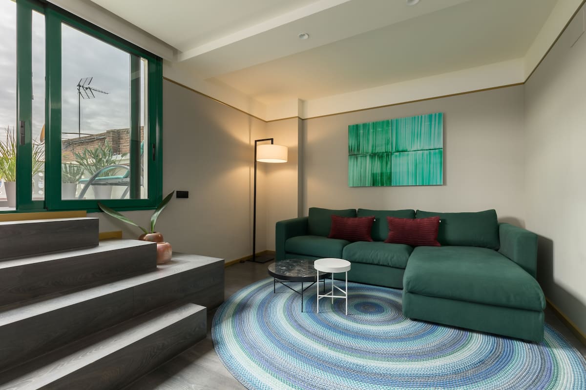 Ein modernes Wohnzimmer mit einem grünen Sofa, einem gemusterten Teppich und einer Treppe, die zu einem Balkon führt.