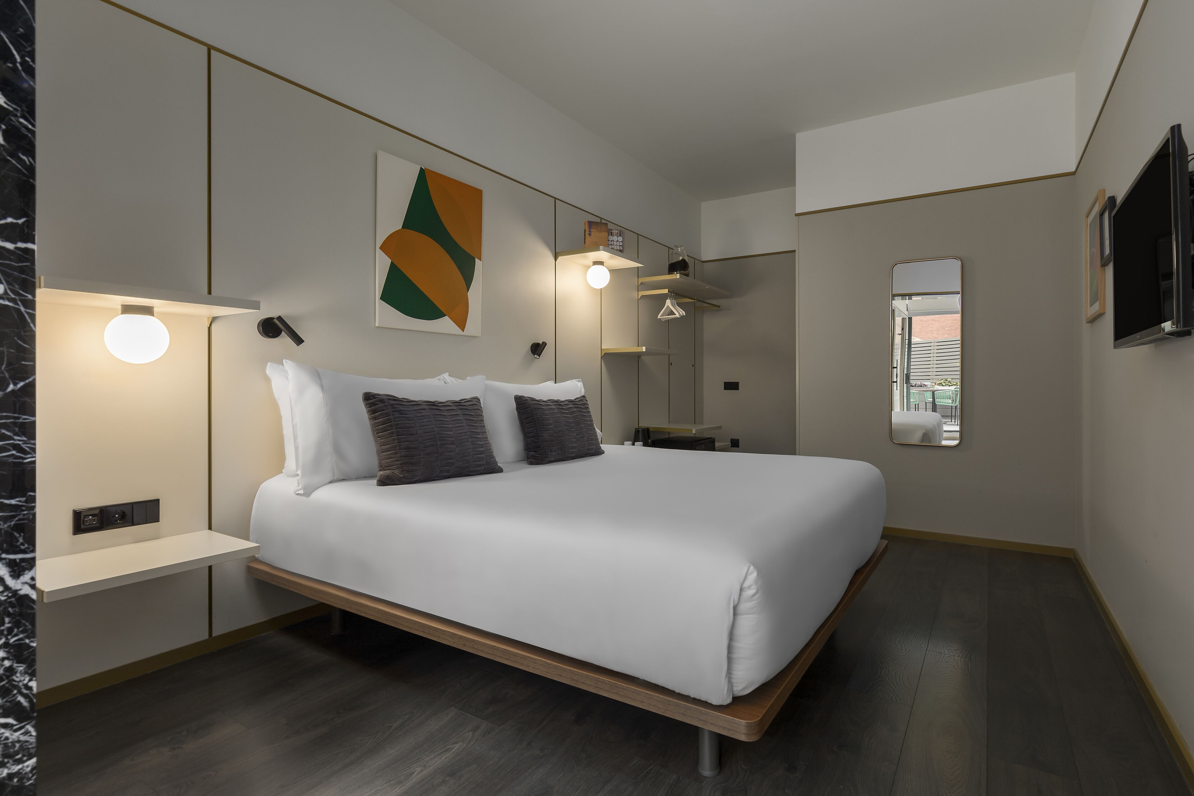 A modern bedroom with a large bed, bedside tables, a wall-mounted TV, and a mirror.