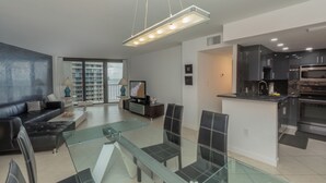A modern living room with a glass dining table, a sofa, and a TV. - Spectacular Gulf views- South Seas Tower 4-1607 (Marco Island)