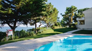 Una piscina con vistas claras al mar, rodeada de exuberante vegetación y un sendero pavimentado.