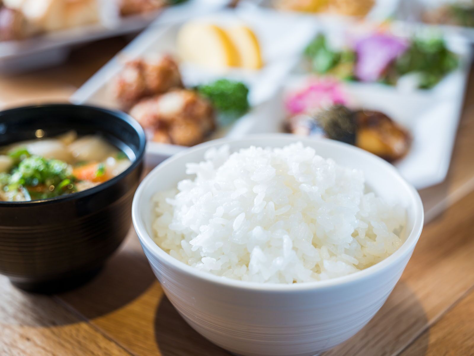 Un tazón de arroz blanco al frente, con un plato de comida al fondo.