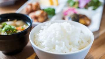 Un tazón de arroz blanco al frente, con un plato de comida al fondo.