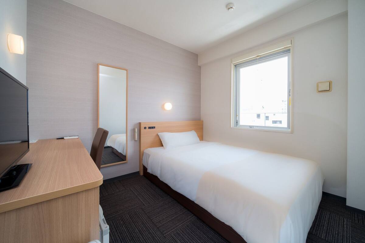 Ein Hotelzimmer mit einem Bett, einem Schreibtisch, einem Stuhl, einem Spiegel, einem Fenster und einer Wandleuchte.