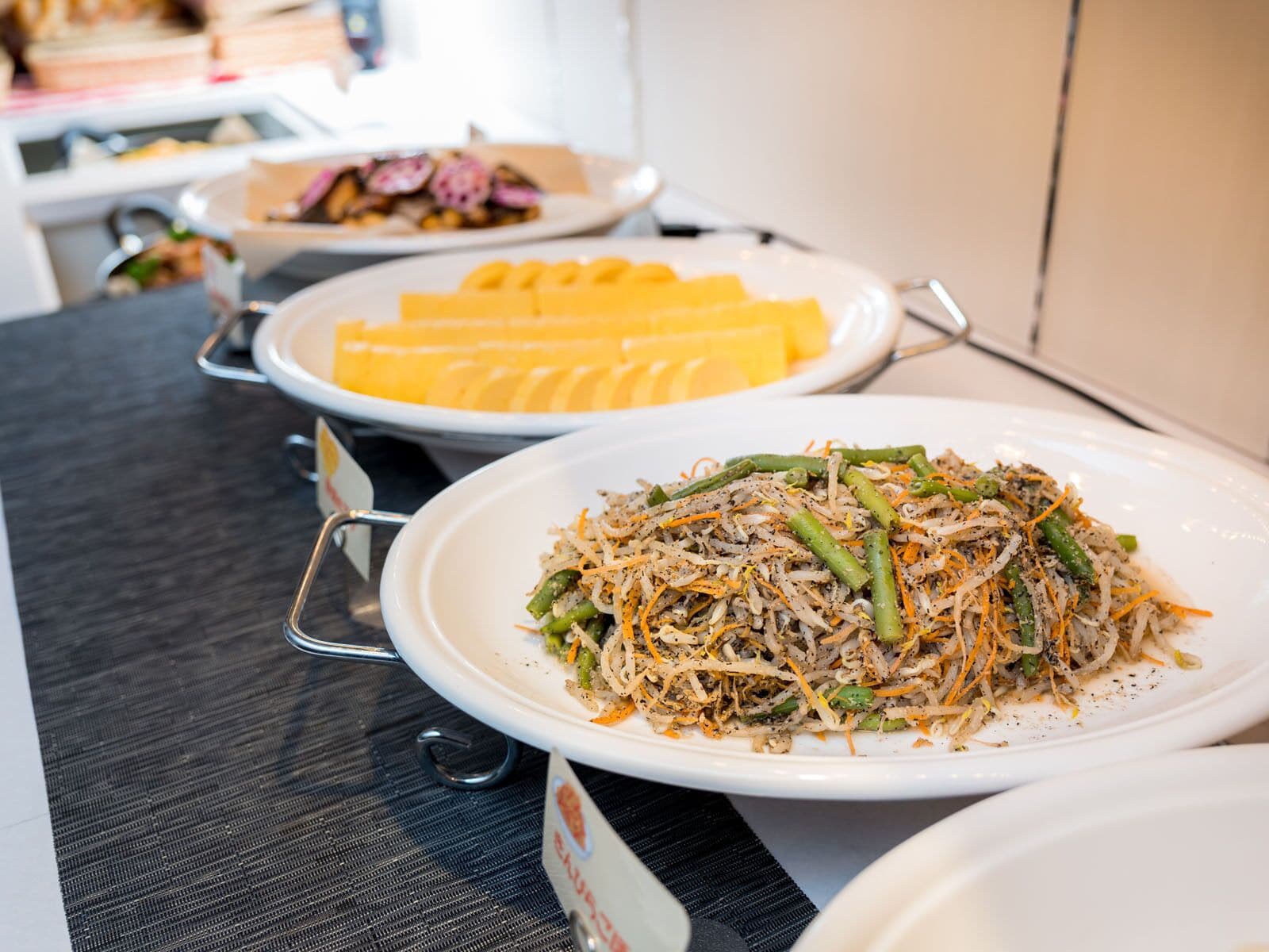 A buffet table with various dishes including a plate of mixed vegetables and shredded cheese.