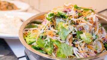 A bowl of salad with various vegetables and shredded cheese.