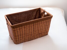 Una cesta de mimbre con asa, sobre una superficie blanca.