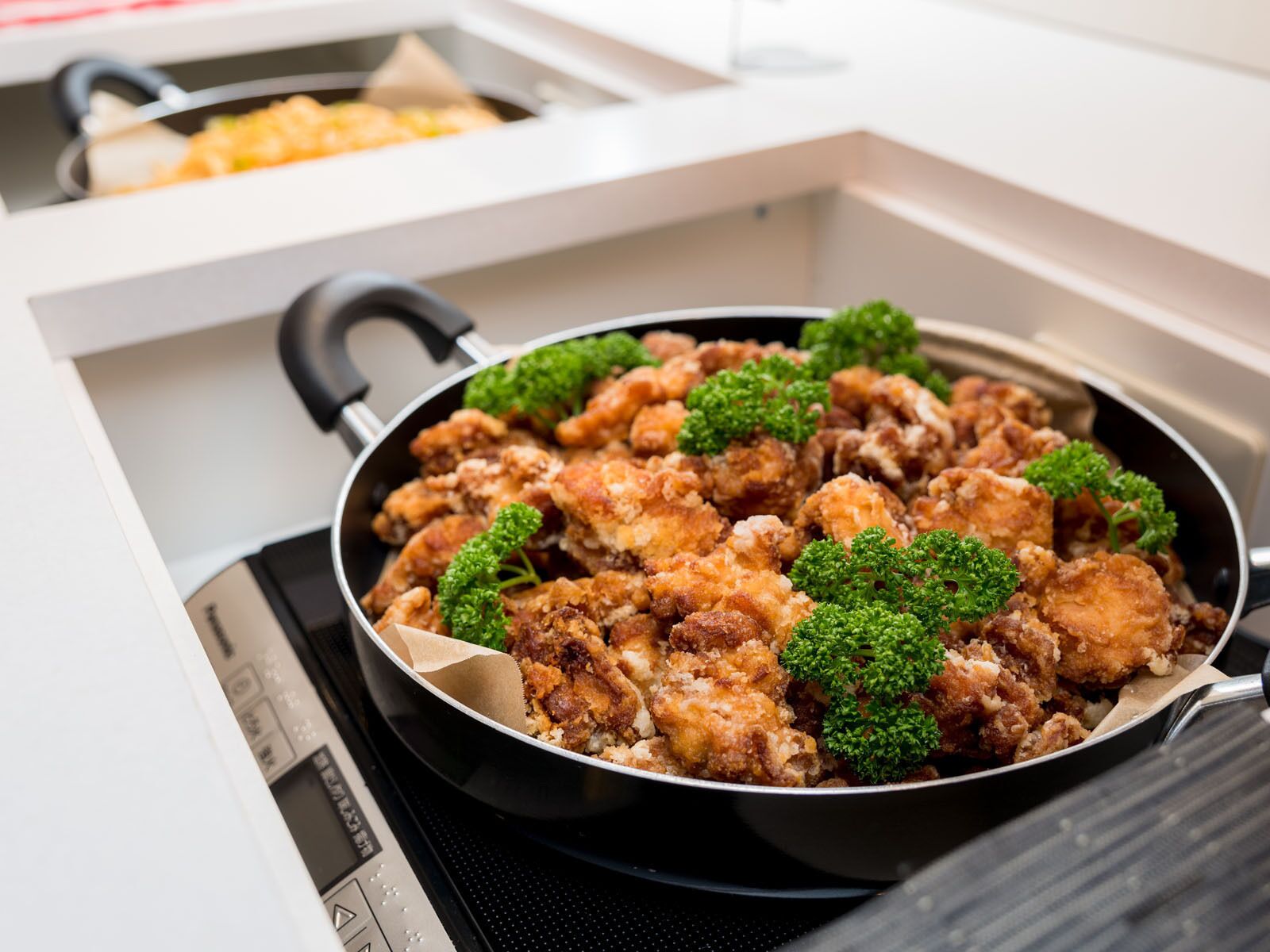 A kitchen with a frying pan on a stove, containing fried food garnished with parsley.