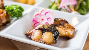 Un plato blanco rectangular con diversos alimentos, incluyendo carne a la parrilla, brócoli y una flor decorativa.
