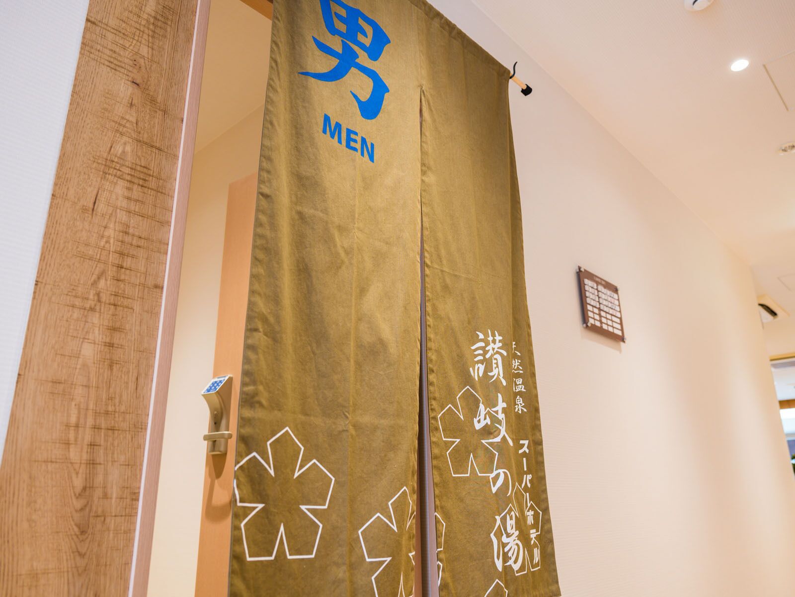 A room with a wooden door, a beige curtain with a blue logo and white text, and a small bulletin board on the wall.