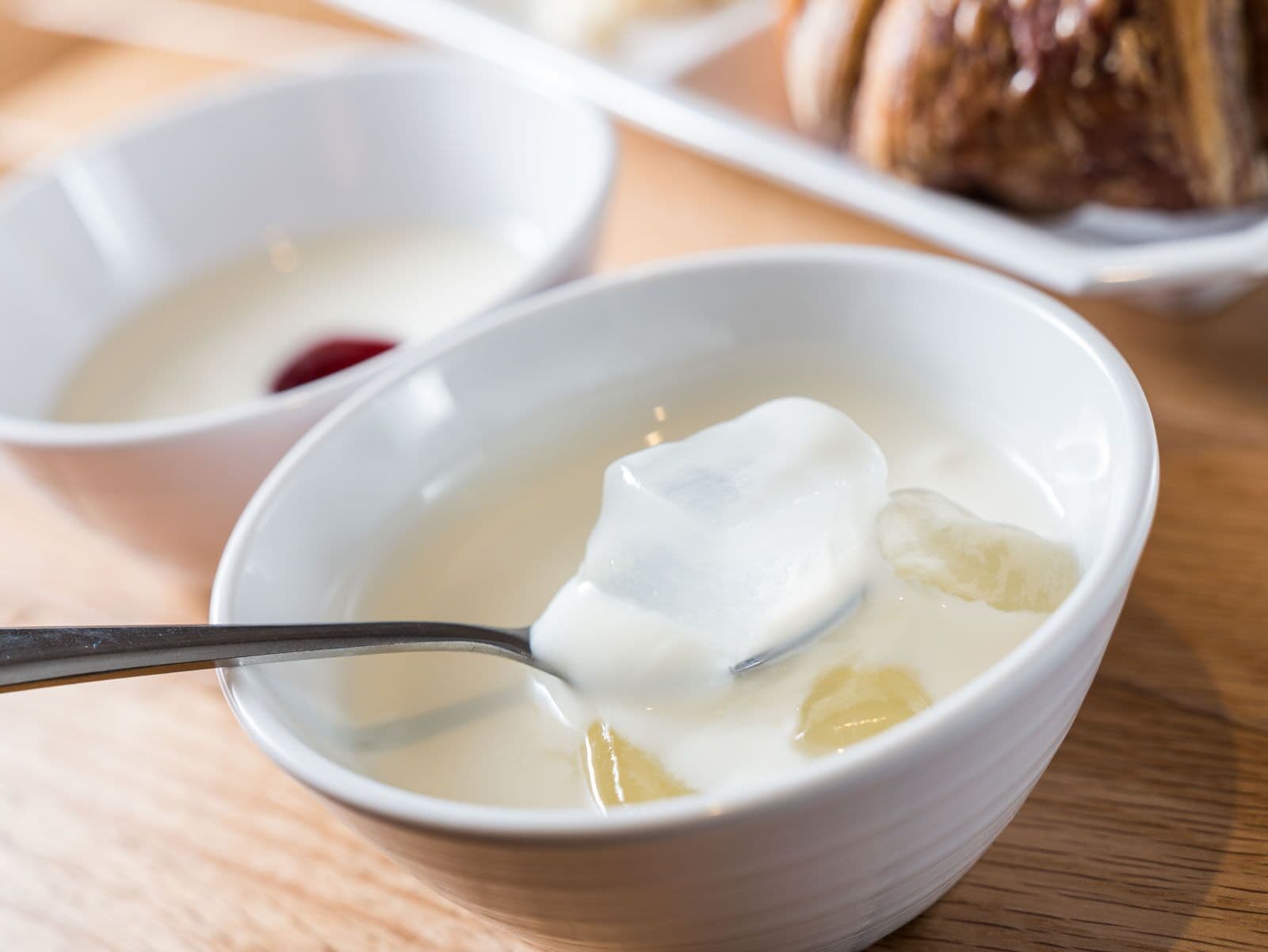 Un bol de soupe avec une cuillère, un petit bol de confiture rouge et une assiette de pâtisseries en arrière-plan.
