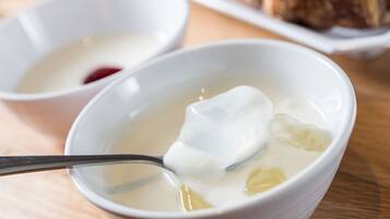 Un bol de soupe avec une cuillère, un petit bol de confiture rouge et une assiette de pâtisseries en arrière-plan.
