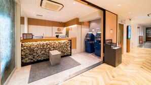 A hotel reception area with a stone wall, a reception desk, and two blue self-service machines. - Super Hotel Takamatsu Tamachi (Takamatsu)