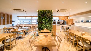 A modern cafe with wooden tables and chairs, a green vertical garden, and a kitchen area visible in the background. - Super Hotel Takamatsu Tamachi (Takamatsu)