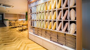 A hotel lobby with a wooden herringbone floor, a reception desk, and a wall displaying neatly arranged pillows and folded towels. - Super Hotel Takamatsu Tamachi (Takamatsu)