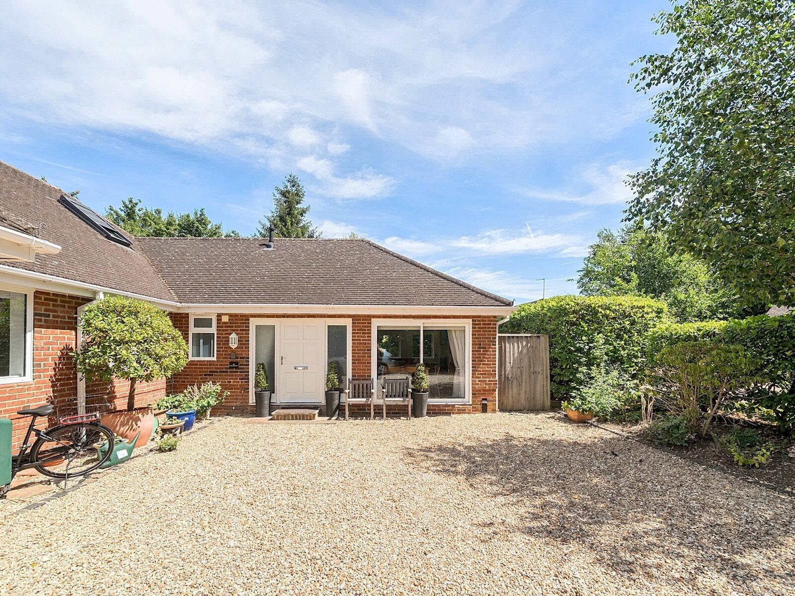 A single-story brick house with a gravel driveway, a patio with a table and chairs, and a bicycle parked outside.