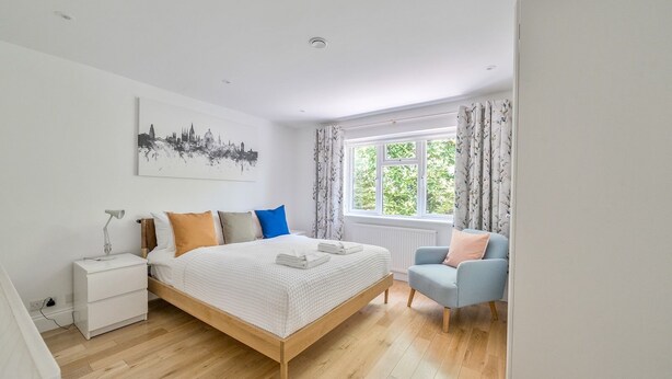 A bedroom with a bed, a chair, a nightstand, a window with curtains, and a cityscape artwork on the wall. - ★ Luxury Oxford Apartment ★ Sleeps 4, Free Parking - Pass the Keys (Oxford)