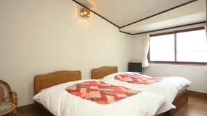 A room with two beds, a wooden floor, a wall-mounted light, and a window with curtains. - Minsyuku Yodoya (Toyooka)