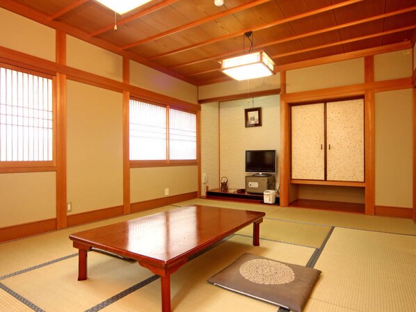 A traditional Japanese room with tatami flooring, a low wooden table, sliding doors, and a television.