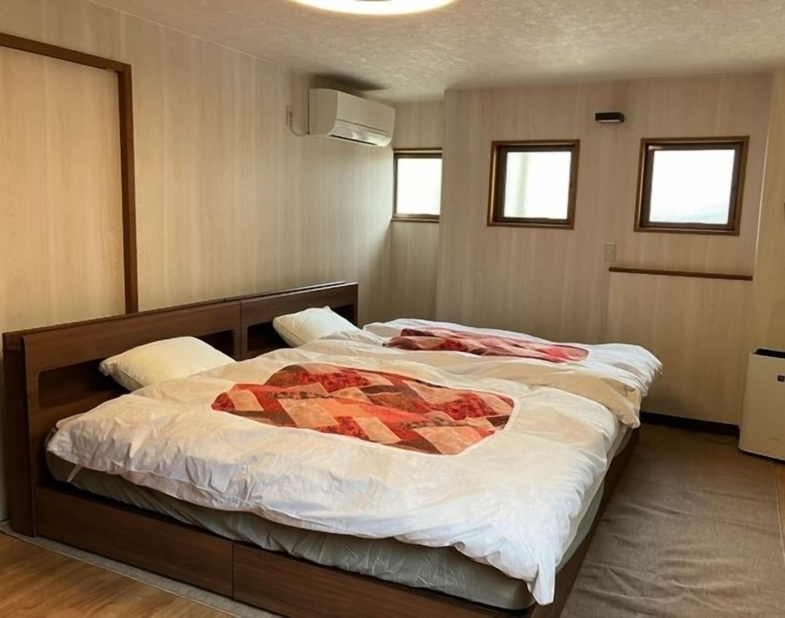 A room with two beds, wooden headboards, a window, and an air conditioning unit.