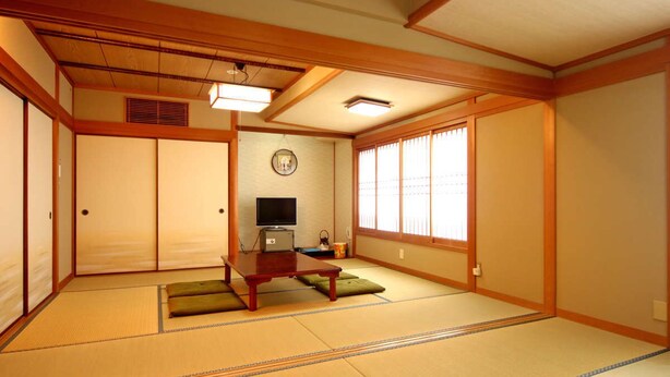 A traditional Japanese room with tatami flooring, sliding doors, a television, and a clock on the wall. - Minsyuku Yodoya (Toyooka)