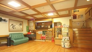 A traditional Japanese room with tatami flooring, a green sofa, a reception desk, and a staircase. - Minsyuku Yodoya (Toyooka)