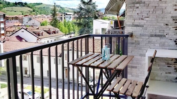 A balcony with a wooden table and chairs, a lantern, and a view of a town with buildings and hills. - VINHOME -Your WINEderful stay in Alba. Apartment in the center of Alba (Alba)