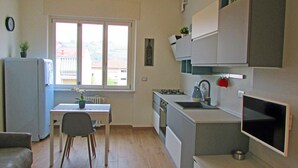 A compact kitchen with a window, a refrigerator, a sink, and a dining area with a chair. - VINHOME -Your WINEderful stay in Alba. Apartment in the center of Alba (Alba)