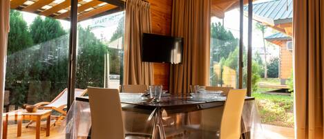 A dining area with a glass table, chairs, and a TV mounted on the wall.