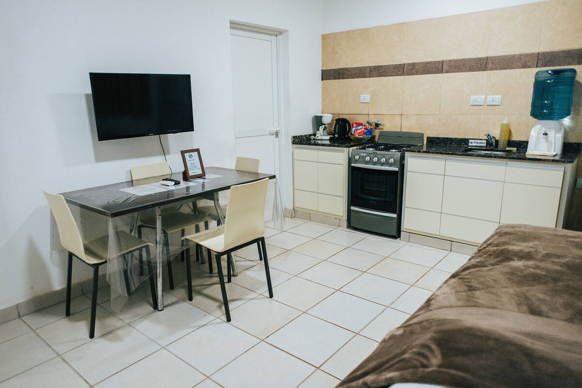 A compact kitchen with a stove, sink, and a flat-screen TV mounted on the wall.