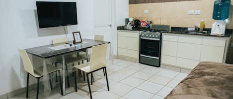 A compact kitchen with a stove, sink, and a flat-screen TV mounted on the wall.