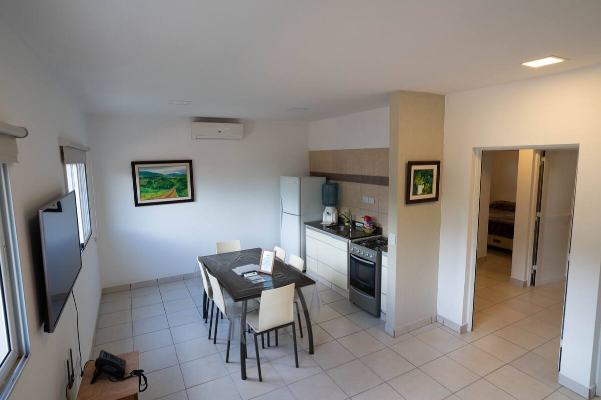 A modern kitchen with a dining area, a flat-screen TV, and a refrigerator.