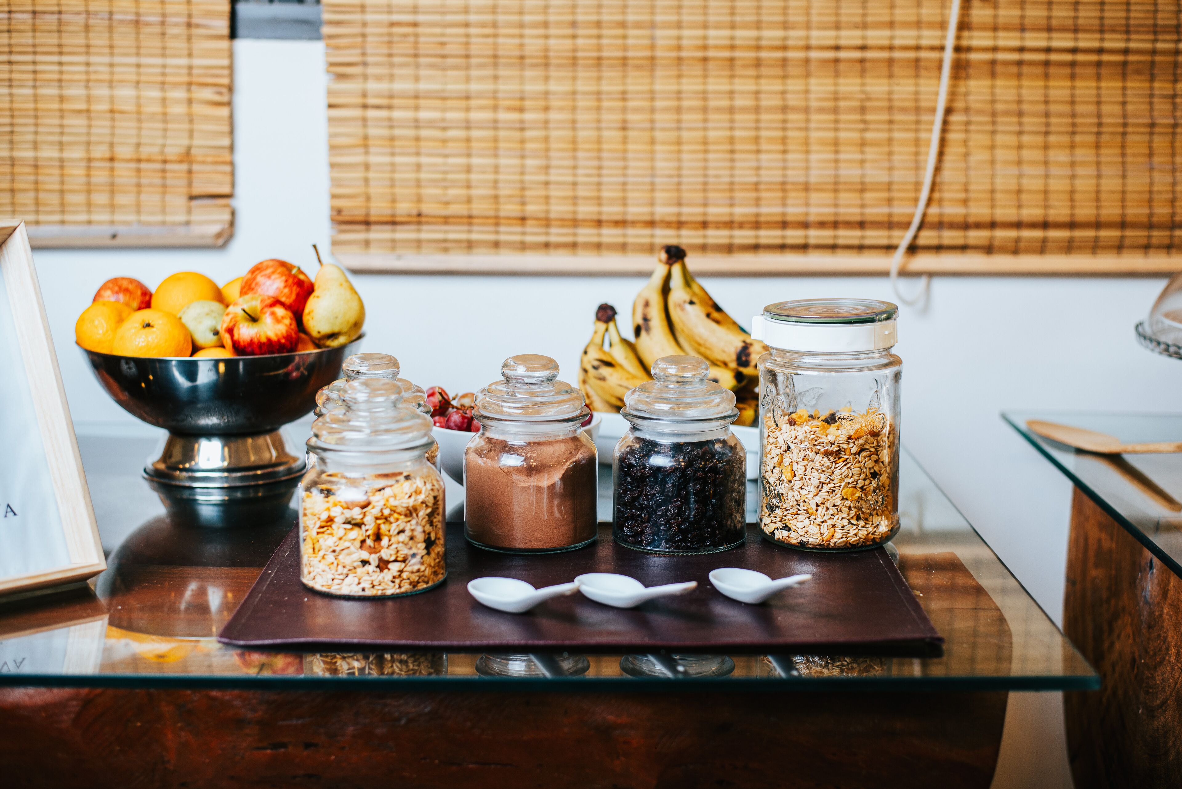 Una barra de desayuno con un tazón de fruta, tres frascos de granola y un racimo de plátanos.