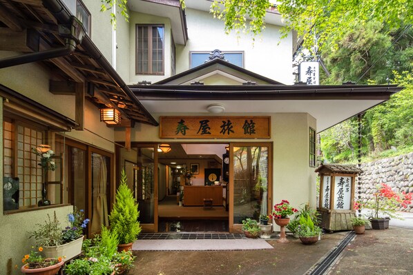 En traditionell japansk byggnad med en träingång, krukväxter och en skylt.