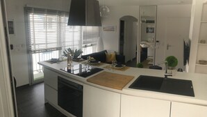 A modern kitchen with white cabinetry, a black countertop, and a built-in dishwasher. There is a dining area with a table set for two, and a small potted plant on the counter. - Appt NEW Arcachon Center, Beach 250 m - Terrace - Private car park (Arcachon)