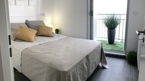 A bedroom with a bed, pillows, a nightstand, a lamp, a potted plant, and a balcony with a railing. - Appt NEW Arcachon Center, Beach 250 m - Terrace - Private car park (Arcachon)