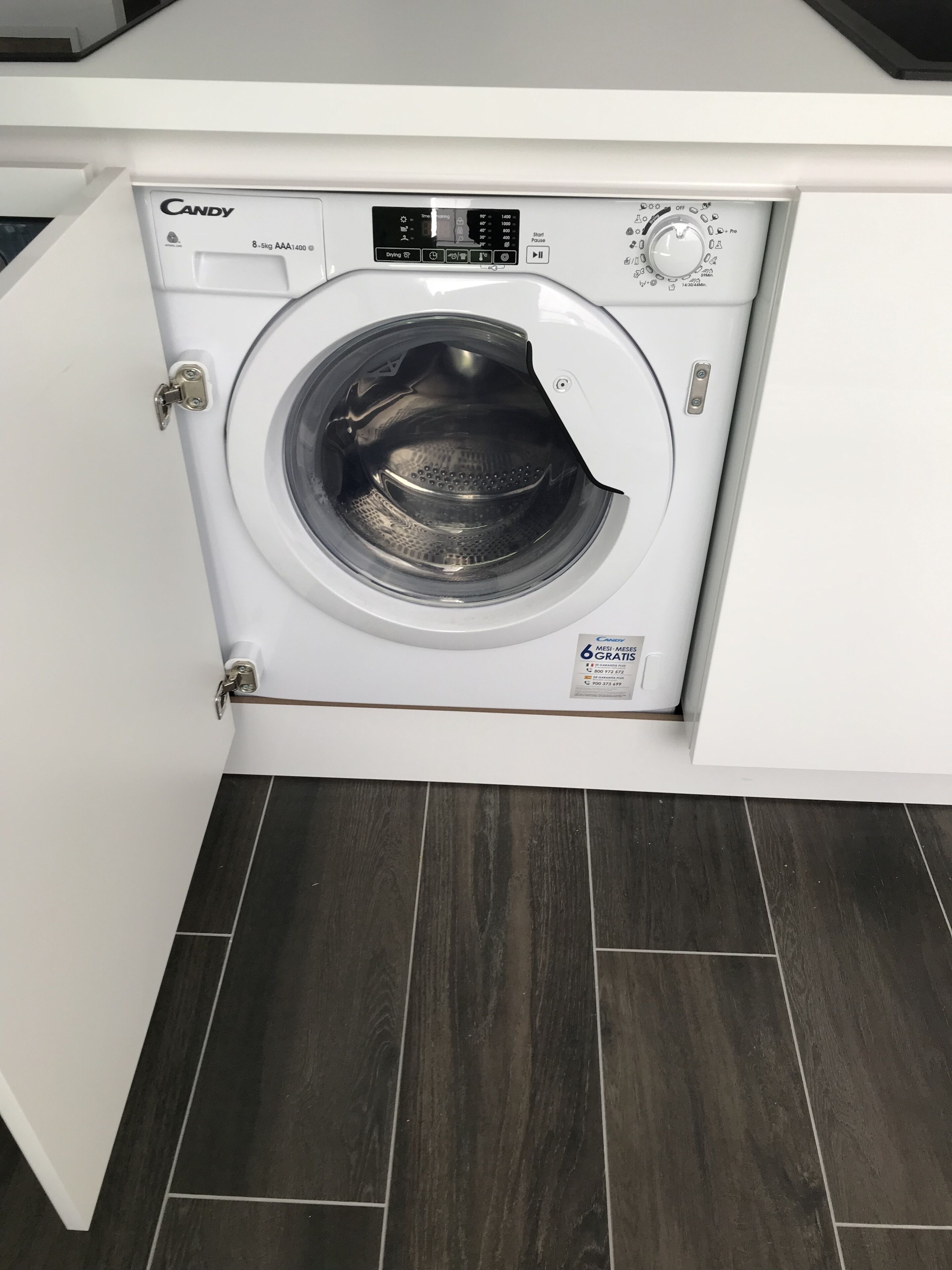Lavadora secadora Candy de carga frontal, con capacidad de 8.5 kg, instalada en un armario blanco sobre un suelo de madera oscura.