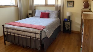 A neatly arranged bedroom with a bed, bedside tables, a nightstand, a clock, and a vase on a cabinet. - Prairie Cottages in historic Rapid City (Rapid City)