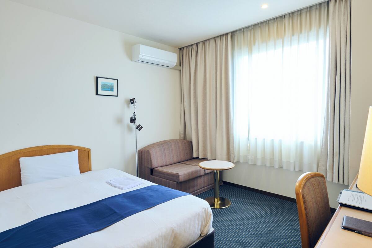 A hotel room with a bed, a sofa, a small table, and a desk with a chair.