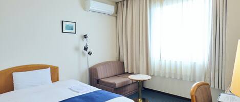 A hotel room with a bed, a sofa, a small table, and a desk with a chair.