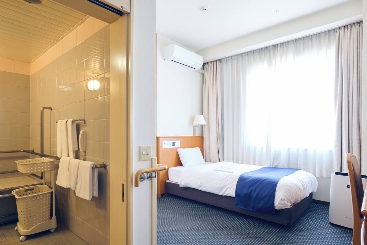 A hotel room with a bed, a bathroom, and a window with curtains.