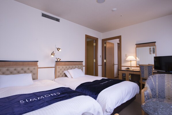 A hotel room with two beds, a desk, a chair, a television, and a mirror.